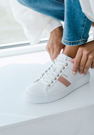 Baskets en cuir blanc avec une surface texturée, des œillets dorés et une bande d'accent rose pâle. Semelle en caoutchouc épaisse avec un design plat.