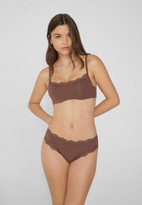 Hnědý bralet s krajkovým lemem a odpovídající kalhotky vyrobené z hladkého materiálu, se zdobným vlnkovým okrajem a jednoduchým designem.