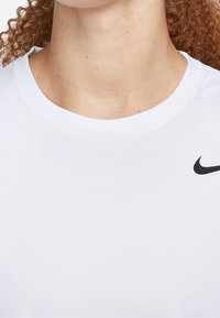 Primo piano di una persona che indossa una semplice maglietta bianca Nike con il logo swoosh nero sul lato destro del petto e capelli ricci rossi in evidenza.