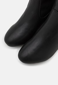 Botines de cuero negro con textura suave, punteras redondeadas y paneles laterales elásticos para facilitar su uso. El diseño es minimalista y elegante.