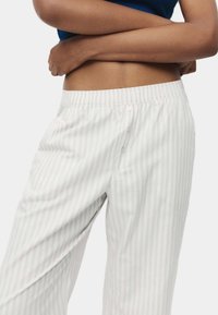 Lichte katoenen pyjamabroek met een subtiel grijs en wit verticale streepjespatroon, voorzien van een elastische tailleband en knoopdetail.