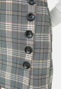 Jupe à carreaux gris avec des rayures marron et blanches, ornée d'une rangée verticale de six grands boutons noirs sur le côté.