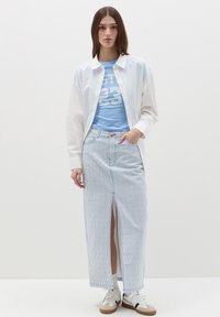 Camicia bianca a maniche lunghe sopra una maglietta grafica blu chiaro con la scritta "23". Gonna di jeans a righe verticali con uno spacco frontale. Sneakers bianche.