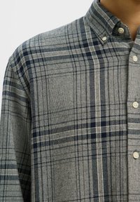 Ruuduline nööpidega särk hallis ja tumesinis, klassikalise kraega, esikäepidemete ja tekstuurse kangaga, millel on erinevad pliidimustrid.