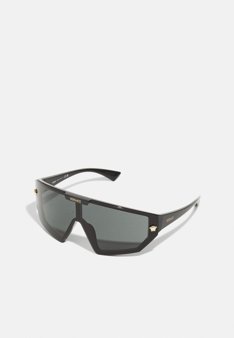 Versace sunglasses with a black plastic frame, oversized angular shape, dark lenses, and gold-tone Medusa emblem on the side.