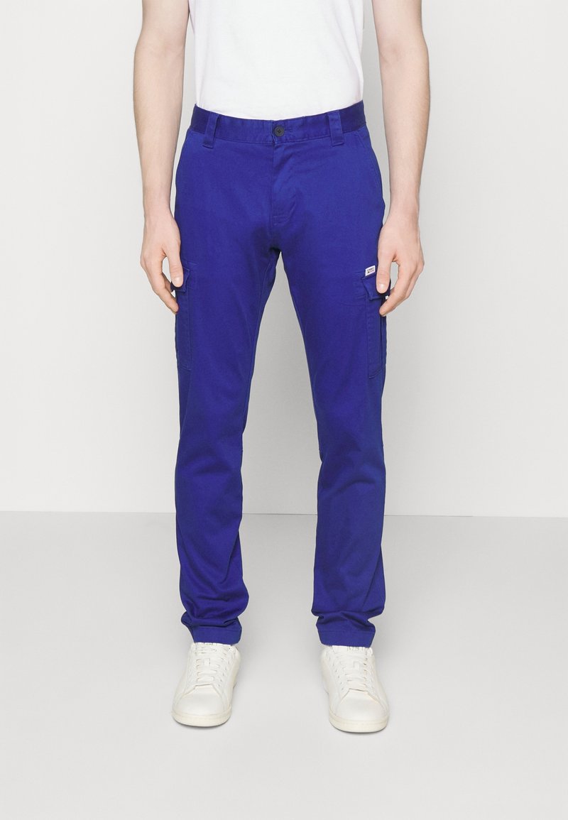 Modré cargo kalhoty s úzkým střihem, vybavené bočními kapsami a zapínáním na knoflík. Vyrobené z odolné tkaniny, v kombinaci s bílými teniskami.