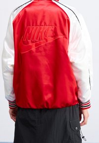 Person som bär en röd och vit satäng Nike-jacka med broderad logotyp på ryggen och en svart cargokjol.