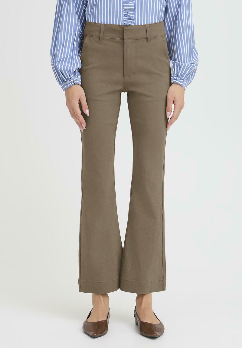 Pantalones acampanados marrones con una cintura alta, hechos de una tela resistente. Presentan un acabado suave y un diseño de bolsillos delanteros. Combinados con zapatos marrones.