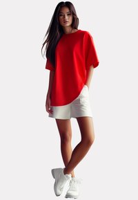 Rode oversized t-shirt met korte mouwen, gecombineerd met witte shorts en witte sneakers. Glad materiaal en een ontspannen pasvorm ontwerp.