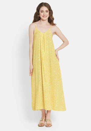 Gelbes Maxikleid mit floralem Muster, aus leichtem Stoff gefertigt. Es hat dünne Träger und einen lockeren Schnitt, stilvoll kombiniert mit goldenen Sandalen.
