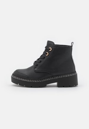 Botines negros de cuero con acabado texturizado, con punta redonda, diseño con cordones, ojales naranjas y suela negra gruesa.