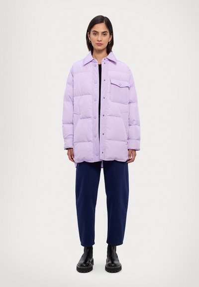 Lavendelkleurige pufferjack met een knoopsluiting aan de voorkant, oversized pasvorm en één borstzak; gecombineerd met donkerblauwe broeken en zwarte enkelboots.