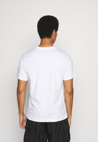 Camiseta de algodón blanca con cuello redondo clásico y mangas cortas, vista desde la parte posterior, que presenta una textura suave y un diseño sencillo.