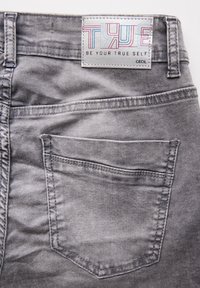 Grijze denim broek met een rechthoekige achterzak en een label met kleurrijke tekst. Glad textuur met een vervaagd waseffect.