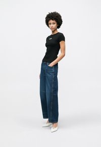 Czarny dopasowany t-shirt z krótkimi rękawami, zestawiony z luźnymi niebieskimi jeansami. Białe szpilki z ostrym noskiem dopełniają strój. Gładki materiał i klasyczny krój.