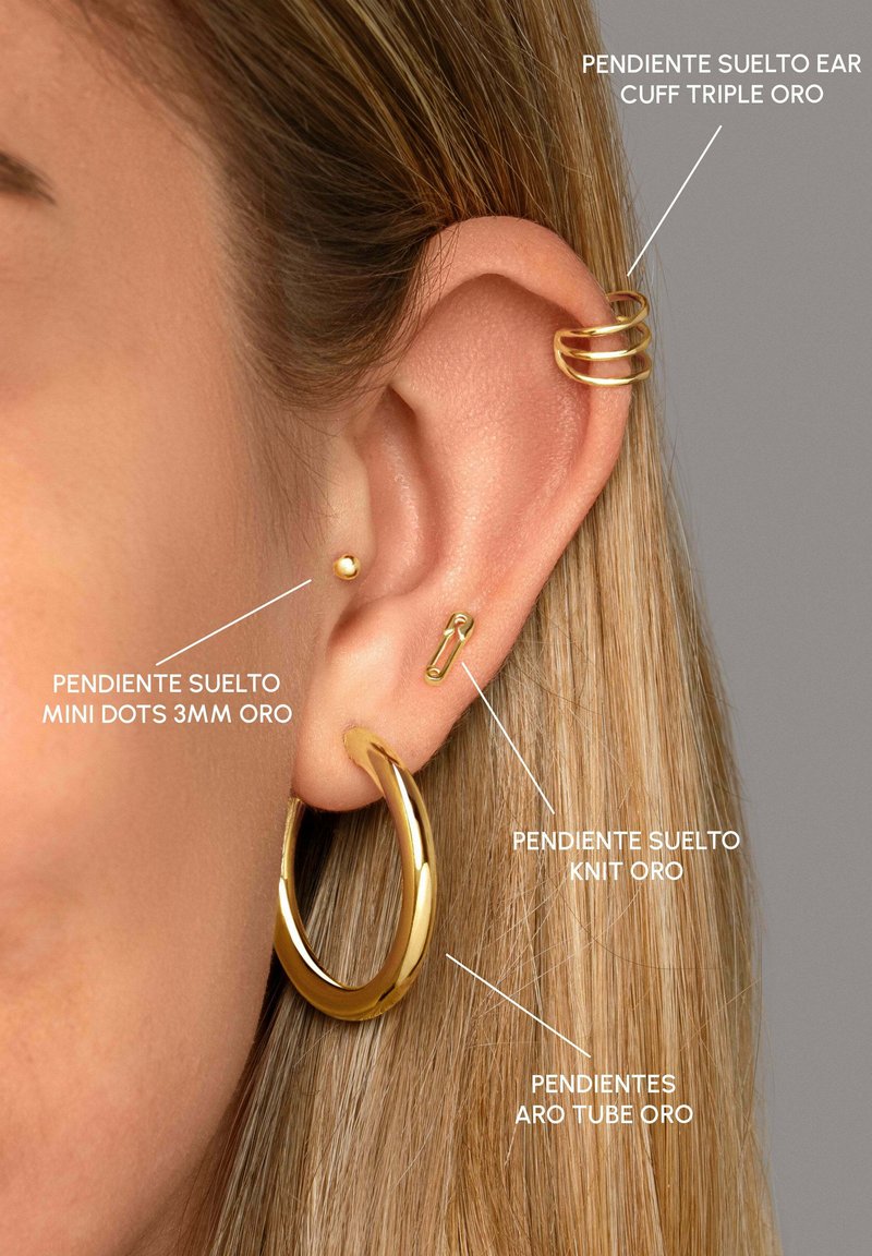 Goldene Creolen mit glatter Oberfläche, goldene Mini-Punkt-Stecker und ein dekorativer Armreif mit drei Ringen, alle an dem Ohr eines Models präsentiert.