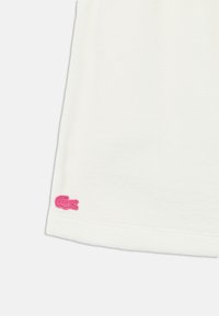 Λευκό πουκάμισο με απαλή υφή, με ροζ κεντητό λογότυπο κροκόδειλου στο τελείωμα. Απλός σχεδιασμός με στρογγυλή λαιμόκοψη.