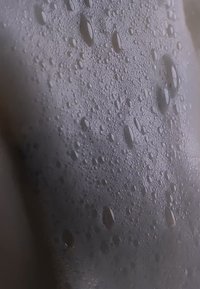 Ingrandimento di una superficie liscia coperta da gocce d'acqua trasparenti e schiuma, che mostra una trama lucida e bolle di dimensioni variabili.