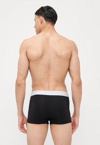 Boxer brevi neri con una fascia elastica bianca, design aderente, texture liscia e taglio a vita bassa. La vista posteriore mostra una vestibilità aderente.