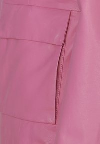 Close-up van een roze leren kledingstuk, met een gladde textuur en een patch pocket met een opgevouwen flap, waarbij de stiksels in detail worden benadrukt.