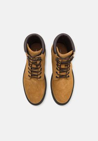 Bottines en suede marron avec des lacets brun foncé, bout rond, col rembourré et extérieur texturé. Semelle en caoutchouc noir avec des coutures décoratives.