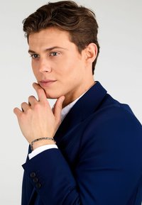 Námornícky modrý oblekový kabát s klopami, nosený cez bielu košeľu. Strieborný náramok na zápästí s prepojeným reťazcom.