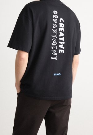 T-shirt en coton noir avec une impression blanche audacieuse "CREATIVE DEPARTMENT" en vertical dans le dos et un petit logo bleu "HUGO".