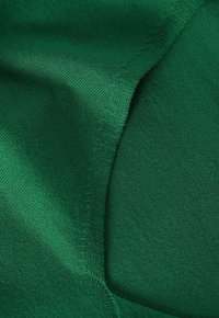 Tessuto verde lavorato a maglia con una texture liscia e una trama uniforme e costante. Il materiale ha una leggera lucentezza e un colore ricco e vibrante.