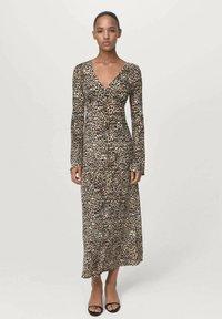 Woman wearing a long-sleeve, V-neck, leopard print maxi dress and black open-toe heels, standing against a plain light background.