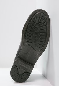 Suola nera di una scarpa con una superficie in gomma testurizzata, motivo di battistrada delineato e dettaglio del logo impresso, con un tacco largo.