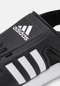 Black slide sandal with white Adidas logo, featuring a textured upper, multiple ventilation holes, and a white sole.