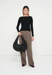 Top negro de manga larga, ajustado en la cintura. Pantalones beige sueltos. Gran bolso negro de tipo slouchy con forma redondeada y textura suave.