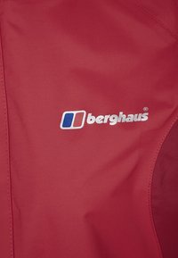 Röd vattentät jacka med en slät yta. Har den vita "berghaus"-logotypen samt blå och vita accenter. Hållbar och lätt design.
