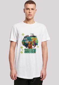 Baltas medvilninis marškinėliai su spalvinga grafinėmis figūromis iš "Scooby-Doo", su užrašu "SCOOB!" ir žalio furgono iliustracija.