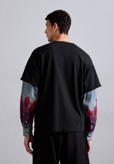 Tricou negru supradimensionat cu mâneci lungi din denim, având un imprimeu cu flăcări roșii. Spatele prezintă un design simplu cu decolteu rotund.