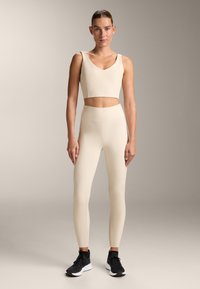 Beige gerippter Croptop und passende hohe Leggings, hergestellt aus dehnbarem Material, kombiniert mit schwarzen Sportschuhen.
