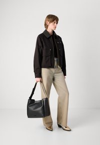 Jachetă scurtă neagră cu accesorii aurii, două buzunare frontale, asociată cu pantaloni largi bej și o geantă de mână din piele neagră, cu un design structurat.
