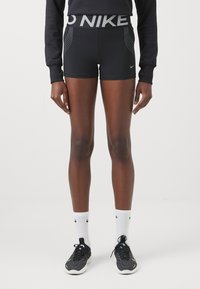Fekete sportnadrág magas derékkal, ezüst színű "NIKE" logóval. Az anyaga rugalmas, sima textúrával rendelkezik és térd felett vágott.