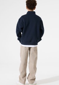 Sudadera navy con cuello alto, fit relajado, puños de canalé, combinada con pantalones sueltos de un beige claro y zapatillas blancas.