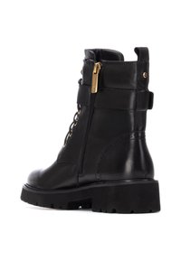 Botas de cuero negro hasta el tobillo con cremallera lateral, diseño con cordones, suela de goma gruesa y adornos decorativos de hardware dorado.