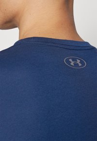 Mjölkblå kortärmad skjorta med en slät textur, med en subtil, cirkulär grå logotyp vid nacklinjen på baksidan.