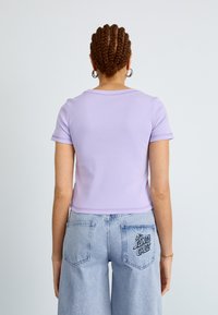 Light purple short-sleeve t-shirt with a rounded neckline and contrasting stitching, paired with light blue wide-leg jeans featuring a logo on the pocket.