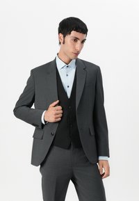 Grå dress med en teksturert stoff, med en mørk vest og lyseblå skjorte. Merkbare detaljer inkluderer knapper og slim fit design.