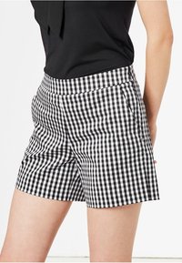 Black and white gingham check shorts with a fitted waist, side pockets, and a smooth fabric texture. Front is shown, with a tuck-in top.