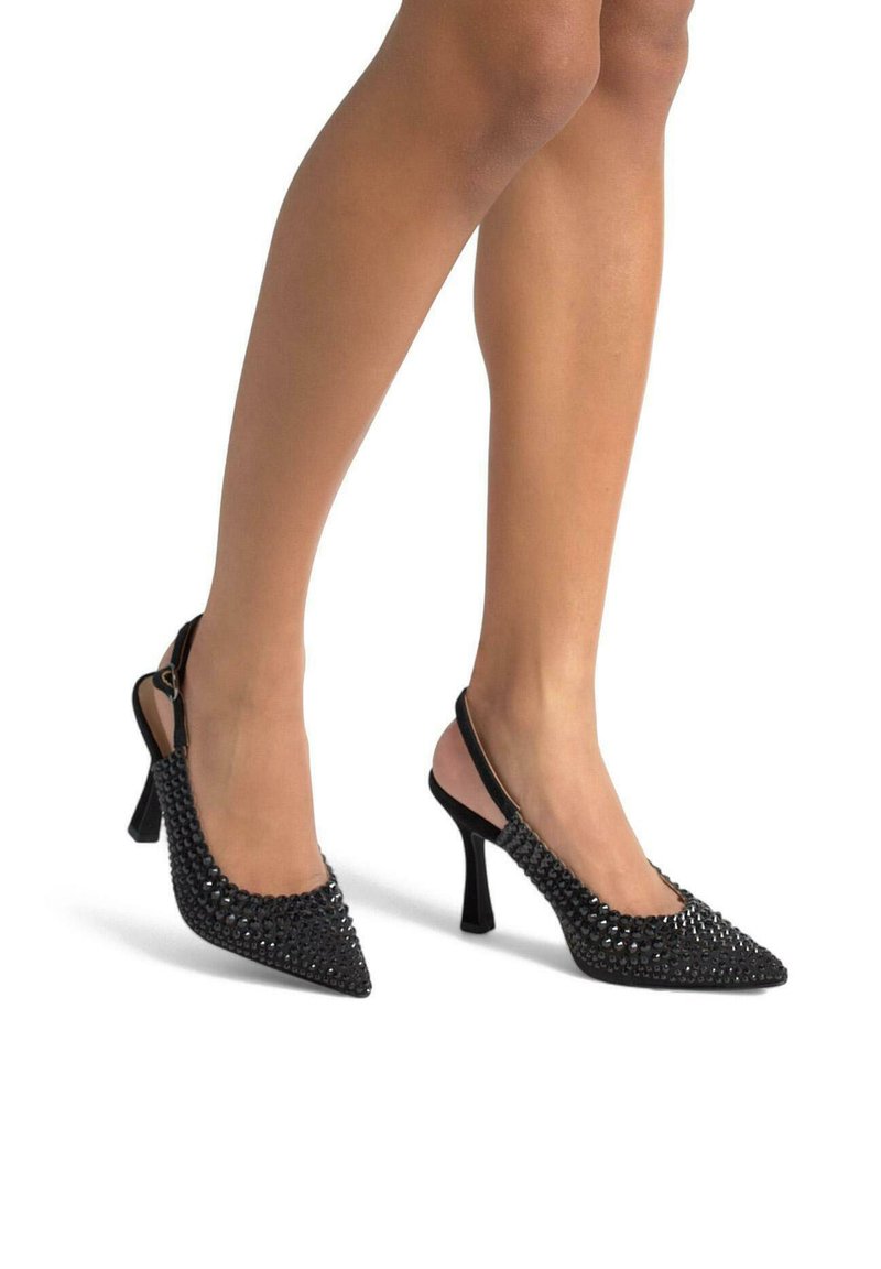 Escarpins noirs à dos nu avec orteils pointus, présentant un design clouté et un talon aiguille. Texture lisse, sangle ajustable à l'arrière.