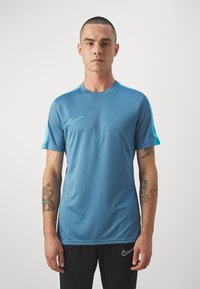 Modré sportovní tričko vyrobené z hladkého materiálu, s krátkými rukávy a kulatým výstřihem. Bílé logo Nike na levém prsu.
