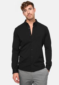 Camisa de botones negra de manga larga con cuello, hecha de una tela suave, con un corte ajustado y mangas de longitud completa.