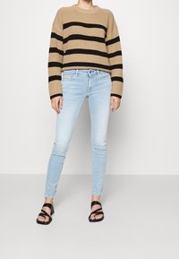 Beige gestreepte gebreide trui met zwarte strepen, gecombineerd met lichtblauwe skinny jeans en zwarte sandaaltjes met bandjes. Gelaagd materiaal en relaxte pasvorm.