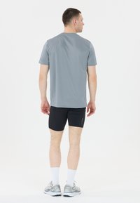 Vaaleanharmaa lyhythihainen urheilupaita, yhdistettynä mustiin shortseihin. Ominaisuudet: sileä rakenne ja yksinkertainen muotoilu, nähtynä takaa.