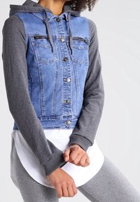Denim jacket blended with gray fabric sleeves and hood. Features button closure, two chest pockets, and a layered white shirt underneath.